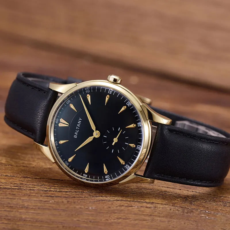 NorthChrono wristwatch featuring a black dial with gold-tone accents, gold hour markers, and a small subdial for seconds. It has a classic leather strap, with the brand name "BALTANY" visible. Set against a wooden surface.