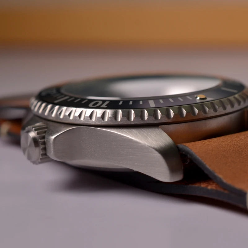 NorthChrono close-up of a dive watch featuring a stainless steel case, black unidirectional bezel with markings, black dial, and prominent crown. Attached is a brown leather strap, suitable for outdoor activities.