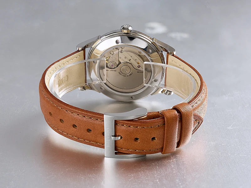 NorthChrono automatic watch with a clear case back showcasing its movement, featuring a brown leather strap with a traditional buckle, set against a metallic surface background.
