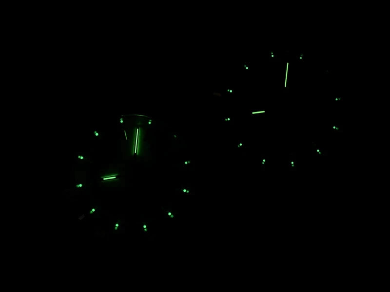 NorthChrono two luminescent clocks displayed in a dark setting, featuring green glowing hands and markers, showcasing their readability in low-light conditions.