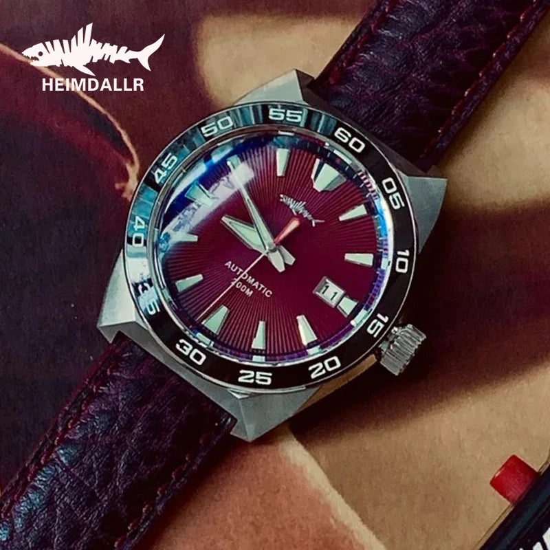 NorthChrono close-up of a HEMDALLR watch featuring a burgundy dial, stainless steel case, rotating bezel, and leather strap. The automatic movement includes a date function and prominent hour markers against a textured background.