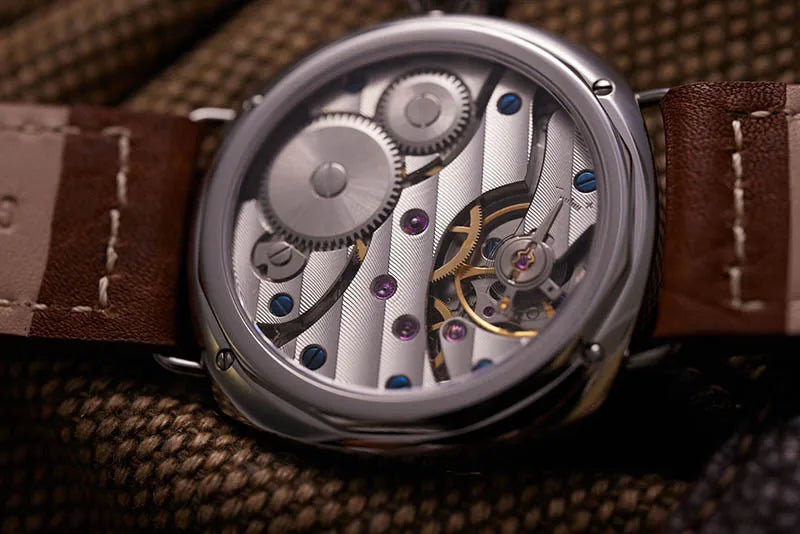 NorthChrono automatic watch caseback view showcasing intricate mechanical movement with visible gears, springs, and colorful jewels. Features a brown leather strap on a textured fabric surface.