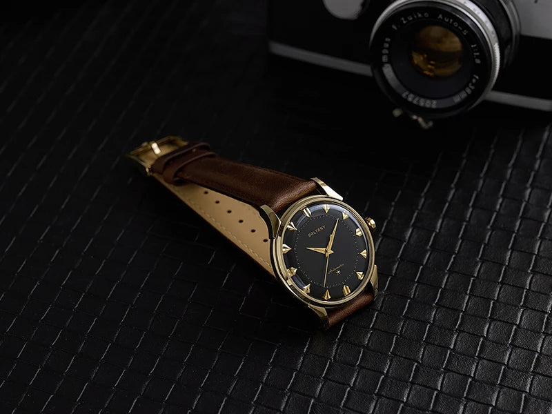 NorthChrono elegant watch featuring a black dial with gold accents and a date window, paired with a brown leather strap. The watch is set against a textured black background alongside a vintage camera.