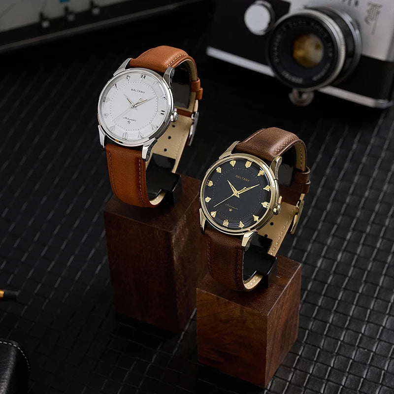 NorthChrono showcases two wristwatches on wooden pedestals: one features a white dial with Arabic numerals and a brown leather strap, while the other has a black dial with applied indices and a brown leather strap, complemented by a vintage camera in the background.
