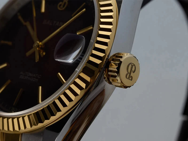 NorthChrono close-up of a luxury automatic watch featuring a black dial, gold-tone markers, gold ridged bezel, and a matching gold crown. The image showcases the fine details of the timepiece.