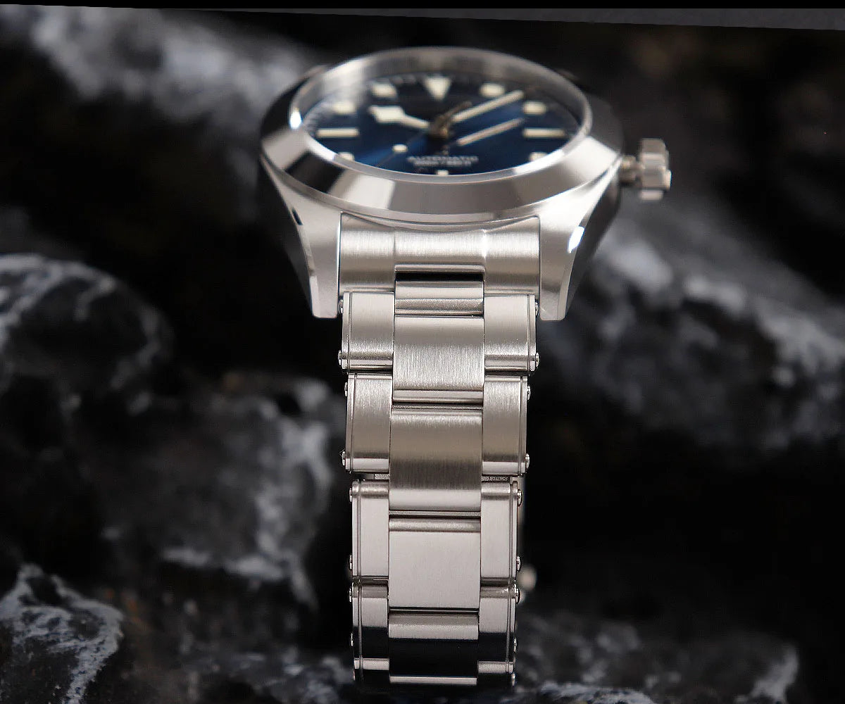 NorthChrono stainless steel watch with a blue dial, round case, hour markers, and date function, displayed on a dark, rocky surface. The metallic band complements the modern, elegant design.