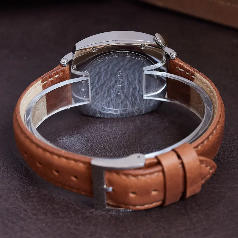 NorthChrono watch caseback view featuring a polished silver stainless steel case and a brown leather strap against a dark leather surface, showing potential model markings.