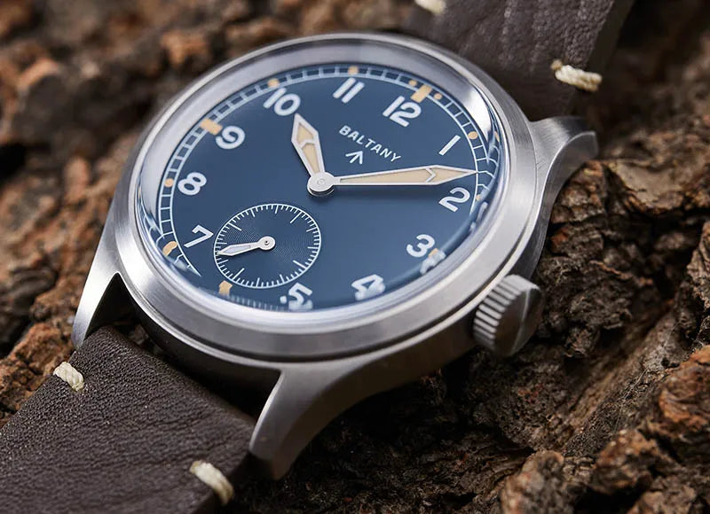 NorthChrono vintage-inspired watch with a blue dial, large clear arabic numerals, and subsidiary seconds dial. It features a stainless steel case and a brown leather strap set against an earthy textured background.