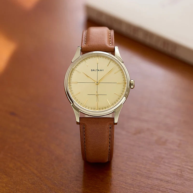 NorthChrono round watch with a light yellow dial and silver-tone accents, featuring the brand name "BALTANY." It has a brown leather strap and is placed on a wooden surface with a book in the background.