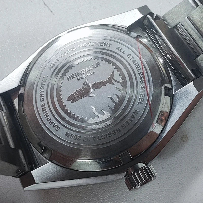 NorthChrono stainless steel watch caseback featuring an engraving of the brand name "HEINDALR," "AUTOMATIC MOVEMENT," "WATER RESISTANT 200M," "SAPPHIRE CRYSTAL," and a fish design, complemented by a stainless steel bracelet.