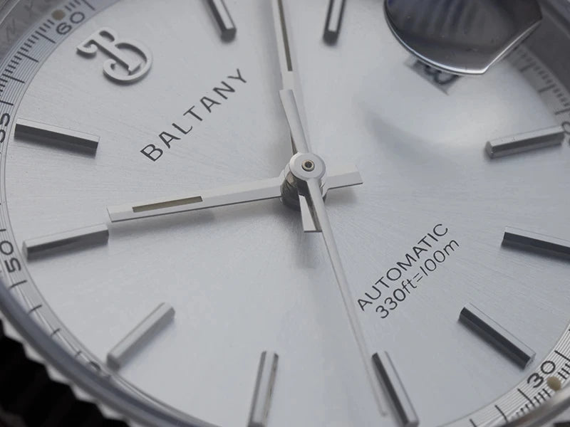 NorthChrono close-up of a BALTANY automatic watch featuring a silver dial with hour markers and hands, indicating water resistance of 330ft/100m, with a magnifying glass reflecting off the surface.