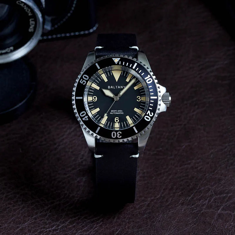 NorthChrono wristwatch with a black dial and silver stainless steel case, featuring a black rubber strap and a rotating bezel. The brand name "BALTANY" is visible, with a vintage camera partially in the background on a textured brown surface.