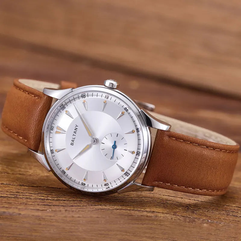 NorthChrono BALTANY minimalist automatic watch with a silver circular dial featuring a white background, silver hour markers, and a seconds subdial. It is paired with a brown leather strap and placed on a wooden surface, ideal for casual or formal wear.