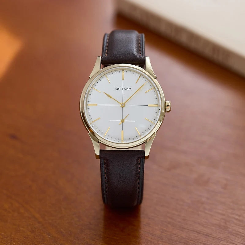 NorthChrono gold-tone watch with a white dial, gold hour markers, and brown leather strap, placed on a wooden surface with a partially visible book in the background.
