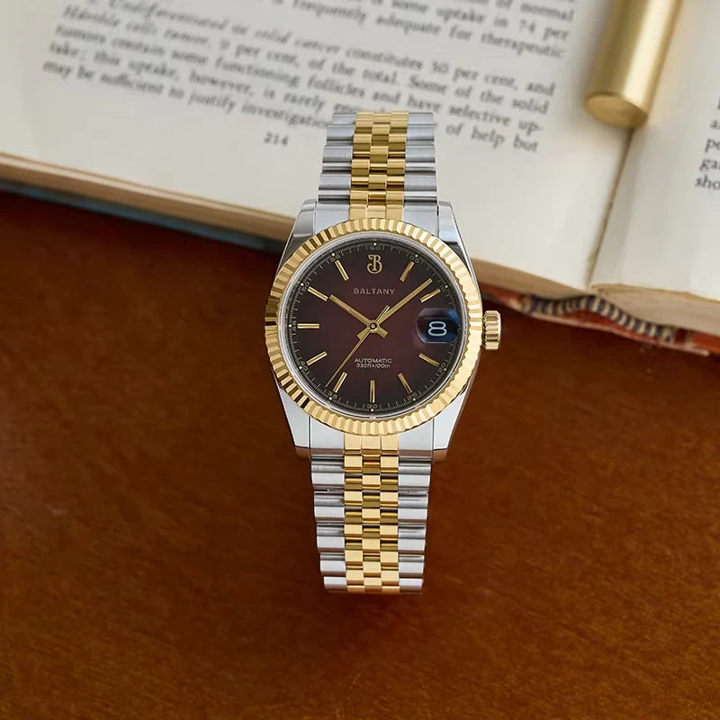 NorthChrono men's watch with a dark brown dial, gold-tone hands and markers, and a date window at 3 o'clock, featuring a two-tone silver and gold metal bracelet, set on a wooden surface with an open book and pen in the background.