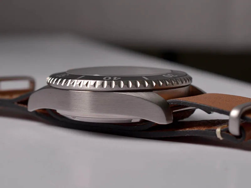NorthChrono metallic watch case with a textured bezel and timing markings, mounted on a classic brown leather strap. Blurred background emphasizes the watch's design and details.