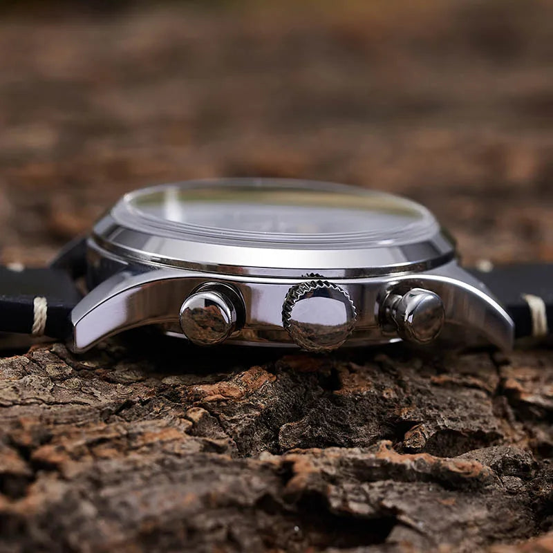 NorthChrono close-up of a classic sporty wristwatch featuring a polished stainless steel case with a round face, black leather strap, and two push buttons. The watch rests on a textured wood surface, showcasing its elegant design.